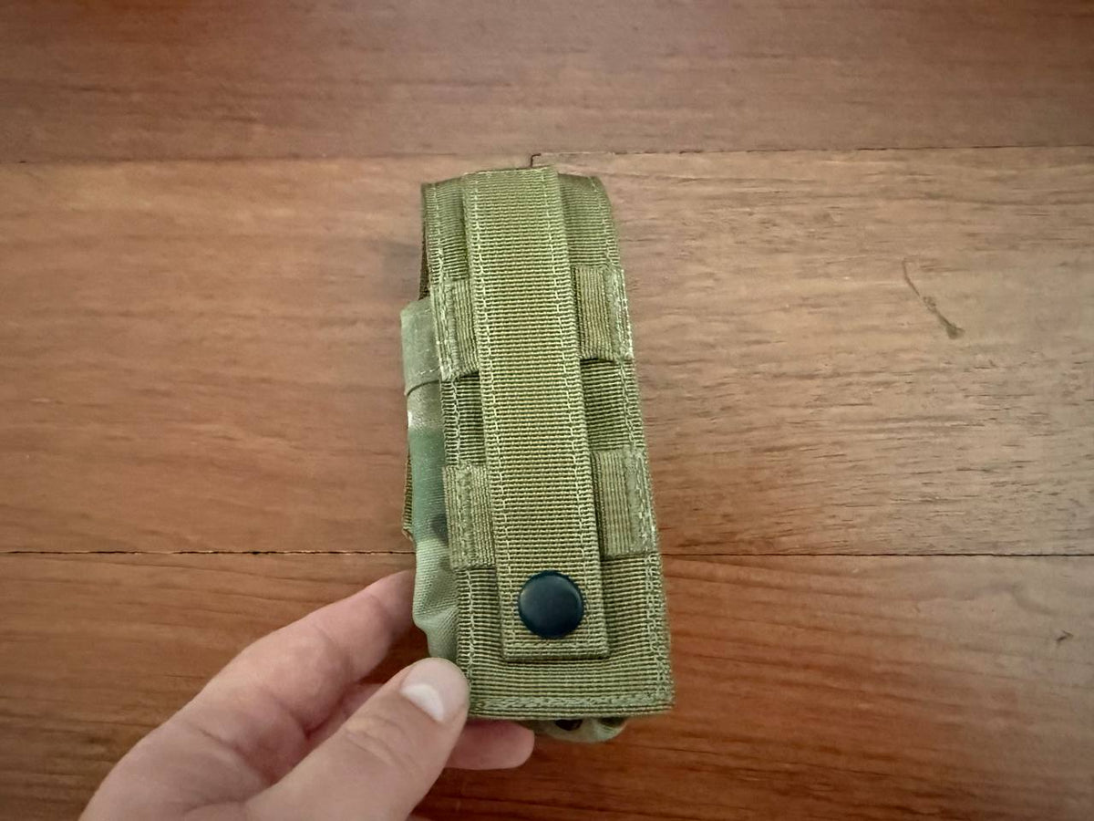 Hand holding a Tactical Single Grenade Pouch - Multicam made of durable fabric with MOLLE attachment on a wooden surface.