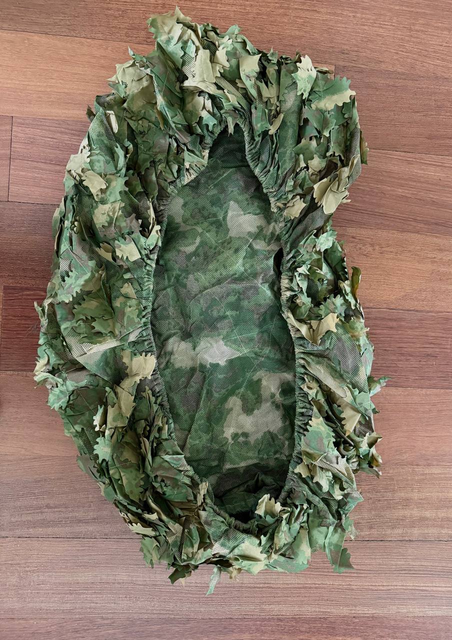 Russian Sokl Leaf Backpack Cover (60L) - Olja Pattern displayed flat on a wooden surface, featuring green and brown leaf-shaped camouflage elements and elastic edges for a secure fit.