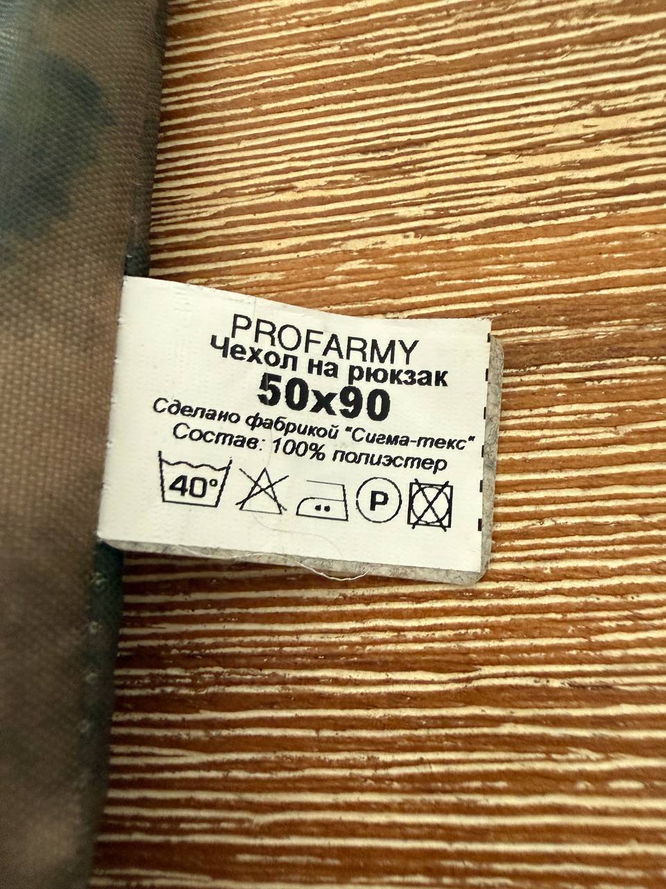 Close-up of the care label on a Russian PROFARMY Waterproof Backpack Cover 30-60L - A-TACS FG Moss, showing washing instructions and material composition of 100% polyester.