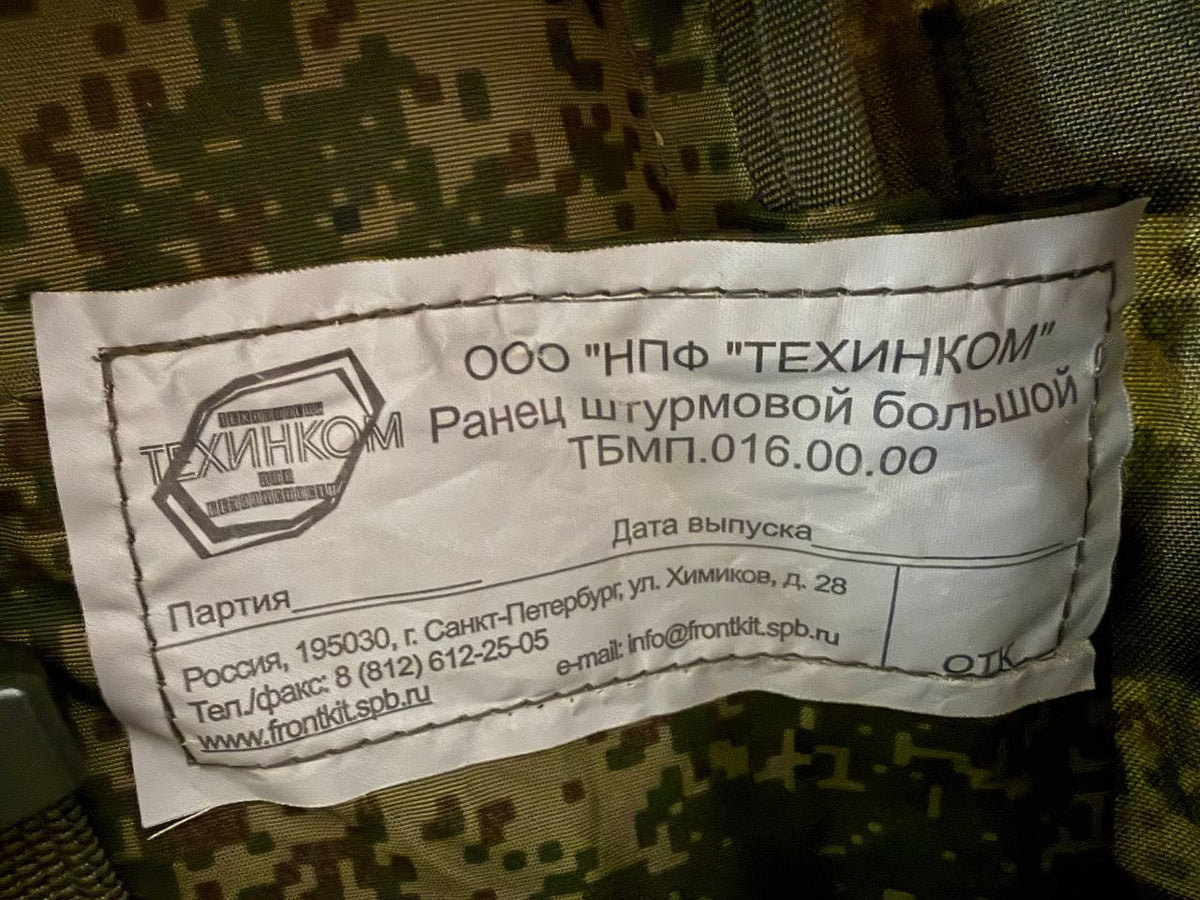 Close-up of a label inside the Russian Tehkinkom Big Assault Backpack - EMR Digital Flora with manufacturer details and contact information in Russian on digital flora camouflage fabric.