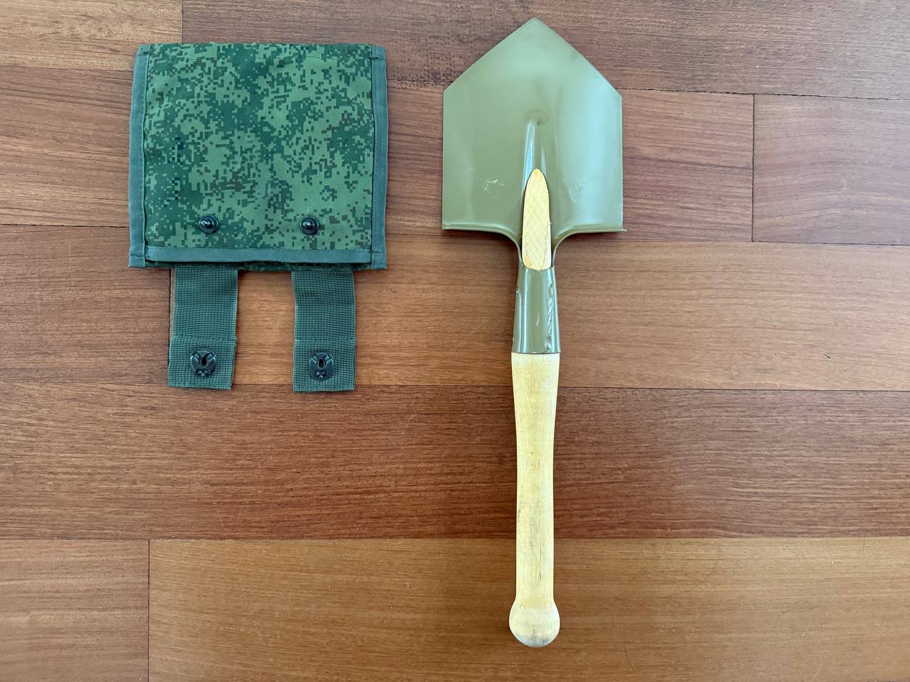 Russian Military Shovel & Tekhinkom Shovel Pouch Set featuring a green metal shovel with a wooden handle and a camouflage fabric pouch on a wooden surface.