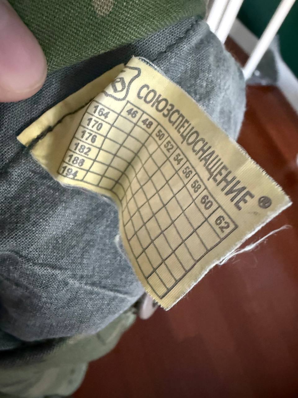 Close-up view of a size label in Cyrillic inside a (USED) Russian SSO Partizan Sever Suit - Size 56-58/5, showing sizing chart and fabric details on gray and green material.