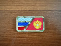 The Russian Tricolor Flag and Emblem Design Patch - Military Badge by Tanki Store features two blue stripes, a red stripe, and a gold double-headed eagle on red. Ideal for buying patches in bulk. Patch shown on a wooden surface.