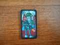 The Russian Futurama Bender Design Patch - Badge by Tanki Store features a cartoon robot in a green hat and jacket holding a rifle with red and blue details, displayed on wood—ideal for collectors seeking quality patches at great prices.